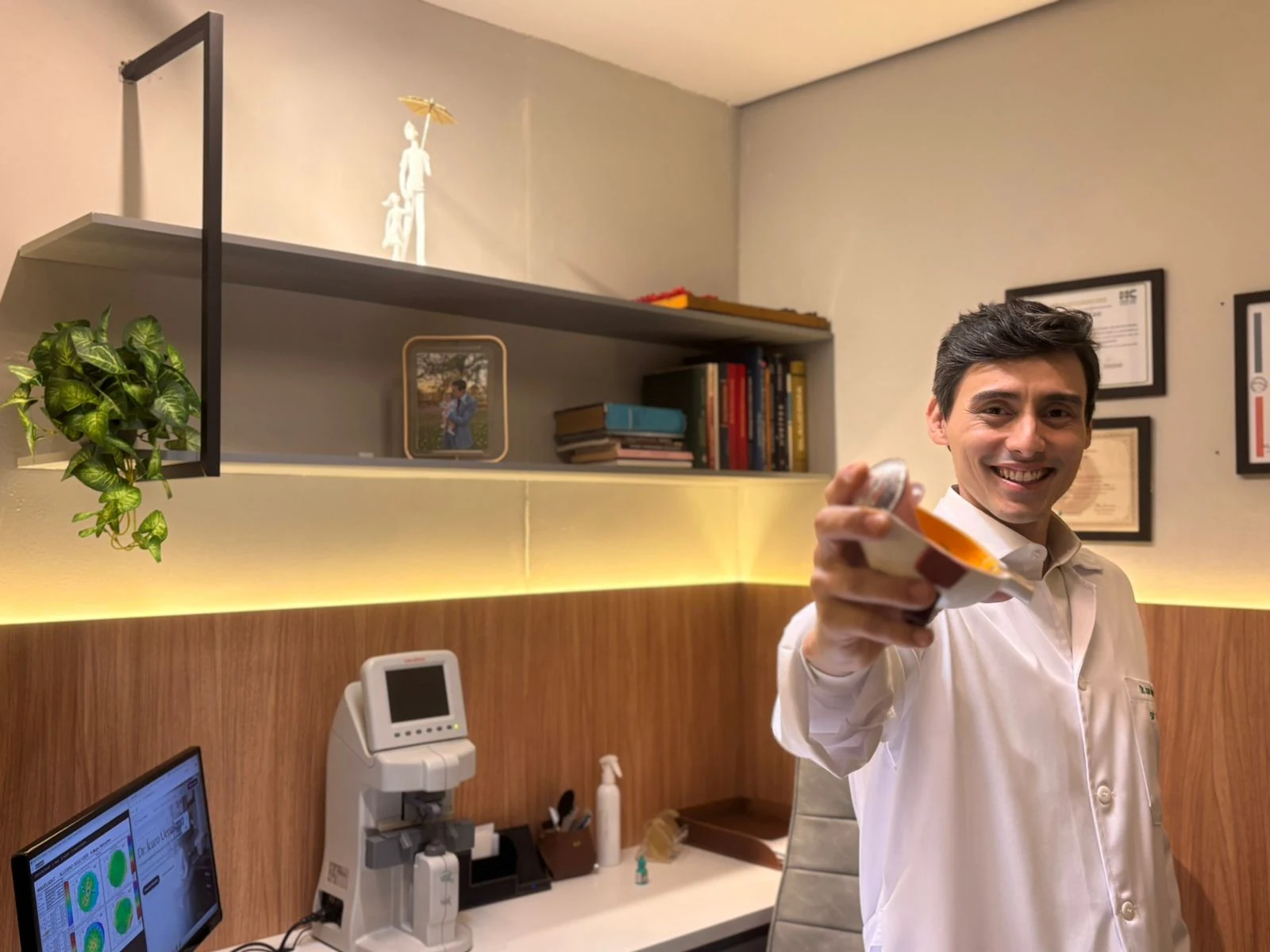 Dr. Ícaro Uenaka em consultório oftalmológico com jaleco e modelo anatômico do olho